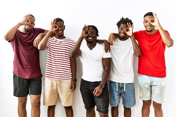 Obraz premium Young african group of friends standing together over isolated background doing ok gesture with hand smiling, eye looking through fingers with happy face.