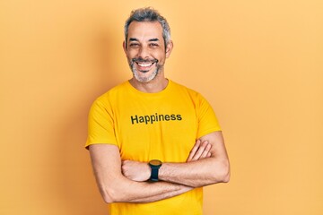 Handsome middle age man with grey hair wearing t shirt with happiness word message happy face smiling with crossed arms looking at the camera. positive person.