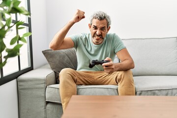 Fototapeta premium Middle age hispanic man playing video game sitting on the sofa annoyed and frustrated shouting with anger, yelling crazy with anger and hand raised