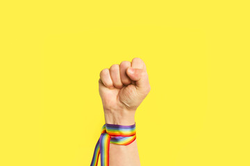 Puño levantado con pulsera de bandera arcoíris LGBT sobre un fondo amarillo brillante liso y aislado. Vista de frente y de cerca. Copy space