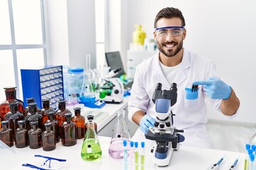 Handsome hispanic man working at scientist laboratory smiling happy pointing with hand and finger