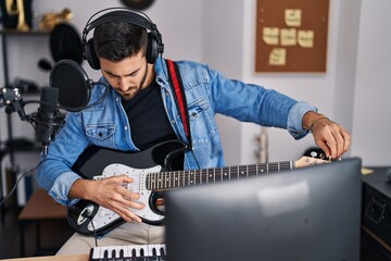Young hispanic man playing electric guitar at music studio