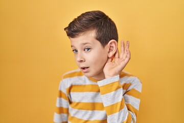 Young caucasian kid standing over yellow background smiling with hand over ear listening an hearing...
