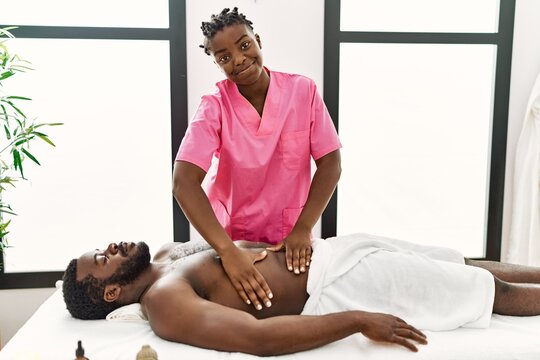 Young physiotherapist woman giving abdominal massage to african american man at the clinic.