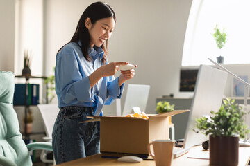 Happy Asian woman packing parcel and taking photo of box