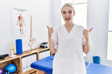 Young caucasian woman working at pain recovery clinic success sign doing positive gesture with hand, thumbs up smiling and happy. cheerful expression and winner gesture.