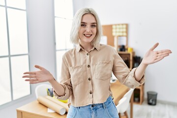 Young beautiful caucasian woman at construction office looking at the camera smiling with open arms for hug. cheerful expression embracing happiness.