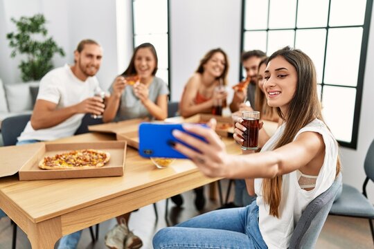 Group of young people smiling happy eating italian pizza and make selfie by the smartphone at home