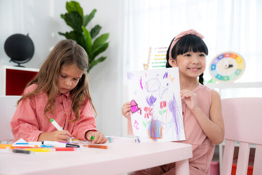 Pretty girls sitting in the kindergarten school classroom and show drawing work to teacher during drawing class. Learning, enjoy, education, playing concept. Feeling happy and fun