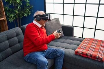 Fototapeta premium Senior man playing video game using virtual reality goggles at home