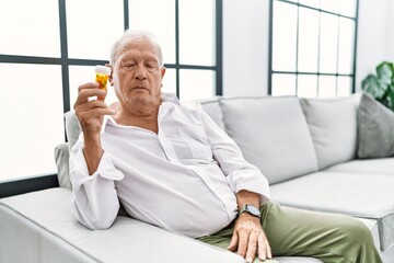 Senior man holding pills relaxed with serious expression on face. simple and natural looking at the camera.