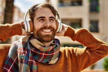 Young caucasian man with beard listening to music wearing headphones outdoors on a sunny day