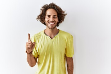 Young hispanic man standing over isolated background showing and pointing up with finger number one while smiling confident and happy.