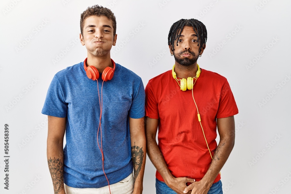 Canvas Prints Young hispanic brothers standing over isolated background wearing headphones puffing cheeks with funny face. mouth inflated with air, crazy expression.