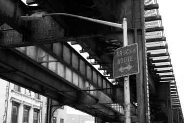 Grayscale shot of an old sign truck route on a light pole under a bridge in Brooklyn, New York