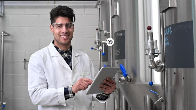Industrial worker technologist in white coat and safety glasses looking at checklist and smiling at camera. Plant worker checking production in food industry. High quality 4k footage