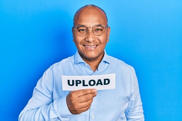 Middle age latin man holding upload paper message looking positive and happy standing and smiling with a confident smile showing teeth