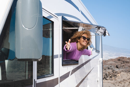 Portrait of beautiful smiling curly woman wearing glasses and violet sweater traveling in motorhome camper looking out the window happy. Caucasian woman enjoying free lifestyle, vacation, travel