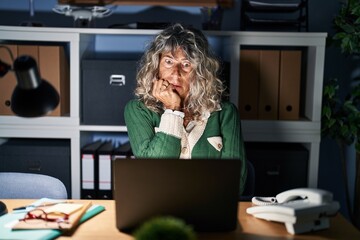 Middle age woman working at night using computer laptop looking stressed and nervous with hands on...