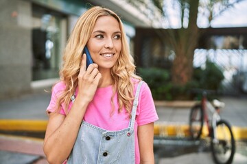 Young blonde woman smiling confident talking on the smartphone at street