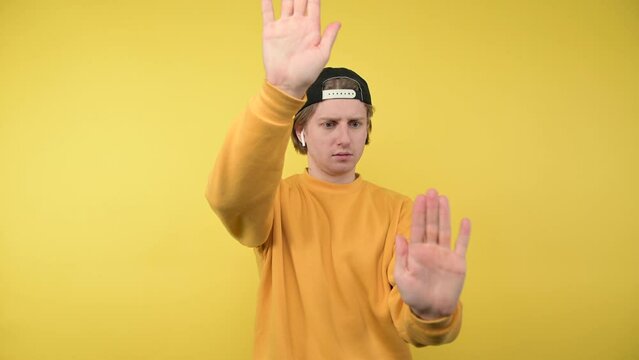Funny mime guy in casual clothes and cap shows a play on a yellow background.