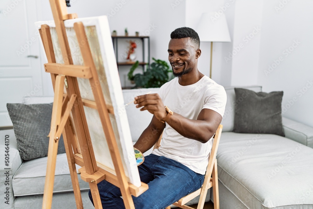 Sticker Young african man painting on canvas at home with a happy and cool smile on face. lucky person.