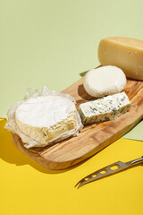 Camembert, blue cheese, mozzarella and pecorino: several cheese sorts on a wooden board on a colorful green and yellow background and a cheese knife