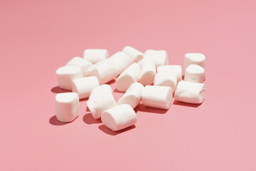 Fluffy white marshmallows in hard light scattered on a pink surface