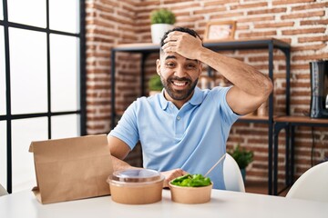 Hispanic man with beard eating delivery salad stressed and frustrated with hand on head, surprised and angry face