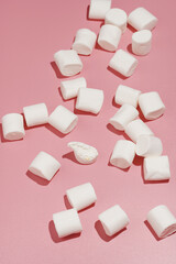 Fluffy white marshmallows in hard light scattered on a pink surface