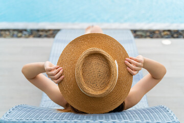 Rearview of a woman in a sun hat relaxing in the swimming pool of a tropical resort luxury hotel