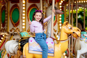 a child girl in an amusement park rides on a carousel and smiles with happiness showing the class,...
