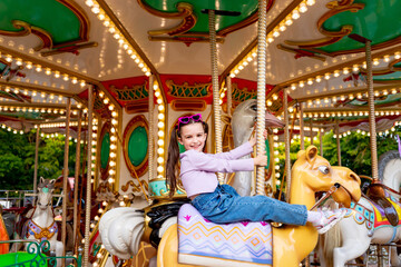 Fototapeta na wymiar a child girl in an amusement park rides on a carousel and smiles with happiness, the concept of weekends and school holidays