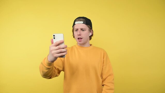 Handsome young man in casual clothes communicates on video with smartphone in hands on yellow background.