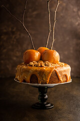 A brown cake with caramel coating and caramelized apples with tree branches on a black cake stand