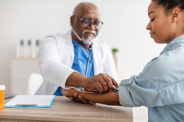 Black male doctor checking measuring pressure on patient's hand