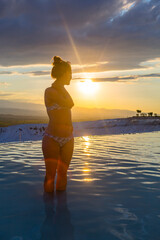 Girl in a bikini enjoying a hot spring pool with calcium-coated cliffs in Pamukkale on sunset