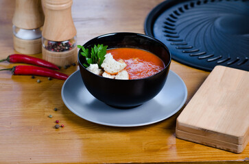 Tomato cold gazpacho soup in a black plate on a wooden table. Cafe or restaurant menu.