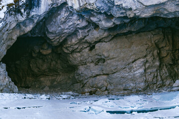 Dark entrance to the cave. View of a gloomy cave on the shore of an icy lake.