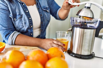 Hispanic brunette woman preparing orange juice at the kitchen