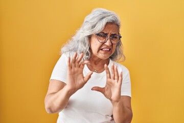 Middle age woman with grey hair standing over yellow background disgusted expression, displeased...
