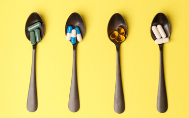 The concept of a healthy lifestyle. Various useful vitamin supplements on a black metal spoon on a yellow background. Close-up, top view. Medical preparations. Treatment of the disease