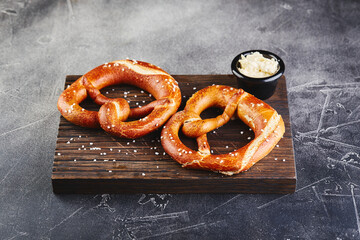 Two pretzels with salt and sauce on wooden cutting board