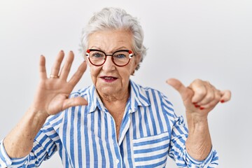 Senior woman with grey hair standing over white background showing and pointing up with fingers number six while smiling confident and happy.