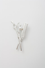 Metallic silver brooch for hairdresser with scissors and comb, pin on white background, bijouterie, jewelry close up