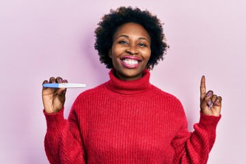 Young african american woman holding thermometer surprised with an idea or question pointing finger...