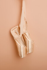 New pink ballet shoes on a pastel color or beige background. Pointe shoes hang on a woman's hand....