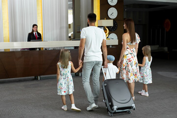 Family of five enters to the hotel lobby to check in at the reception for vacation