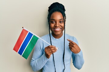 African american woman with braided hair holding gambia flag smiling happy pointing with hand and...