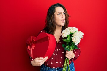 Young caucasian woman holding valentine gift and flowers angry and mad screaming frustrated and furious, shouting with anger. rage and aggressive concept.